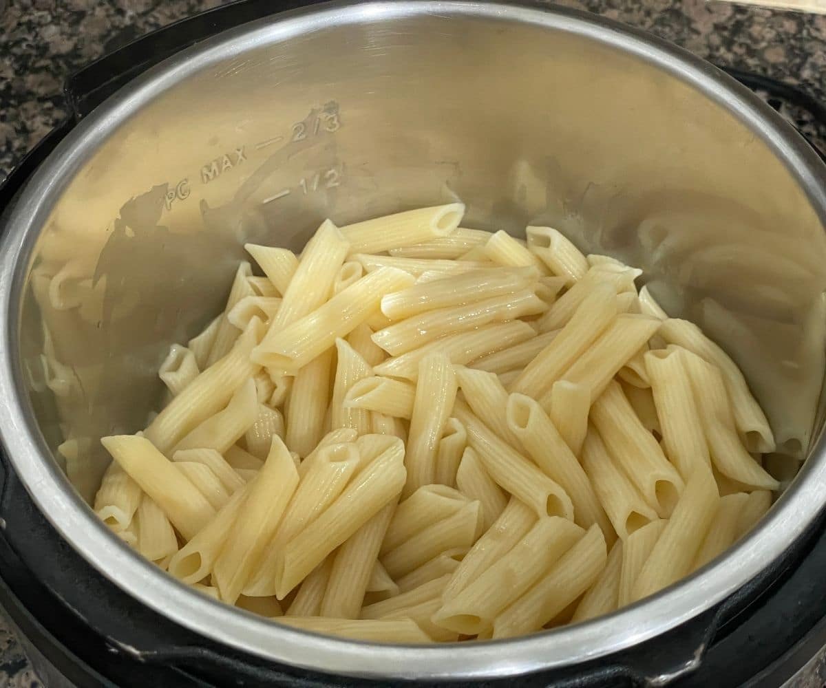 An Instant pot is with cooked Penne pasta.