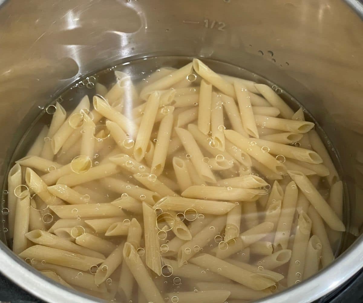 An instant pot is with Penne pasta and water.