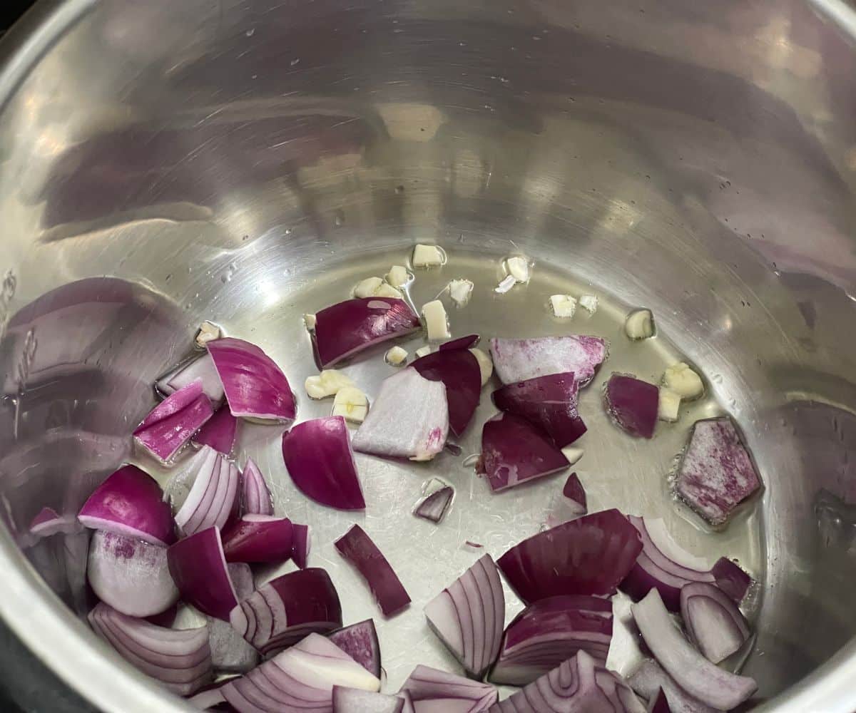 An instant pot is with onions and garlic for zucchini soup.