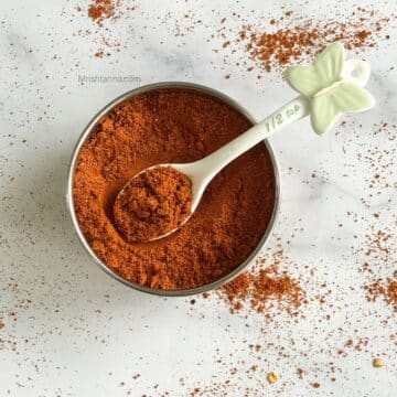 A bow of madras curry powder is on the table a spoon is inserted.