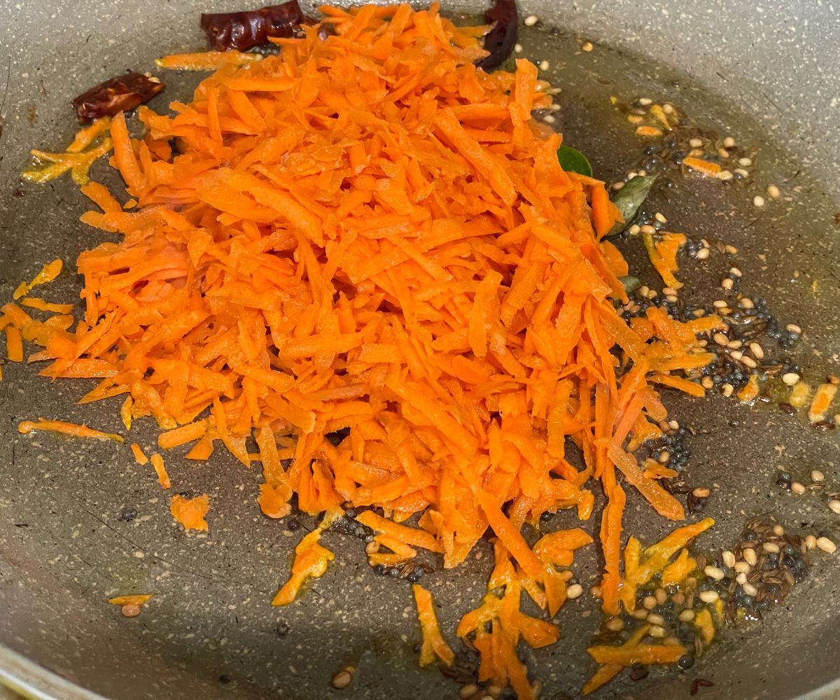 A pan is with spices and grated carrots over the flame.