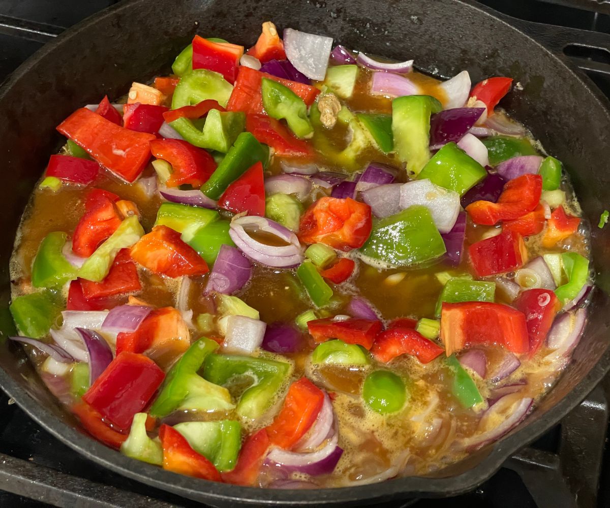 A pan is with bell peppers and onions and hot sauce for stir fry.