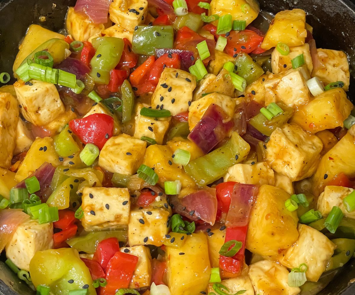 Pineapple tofu stir fry is on the skillet topped with green onions.