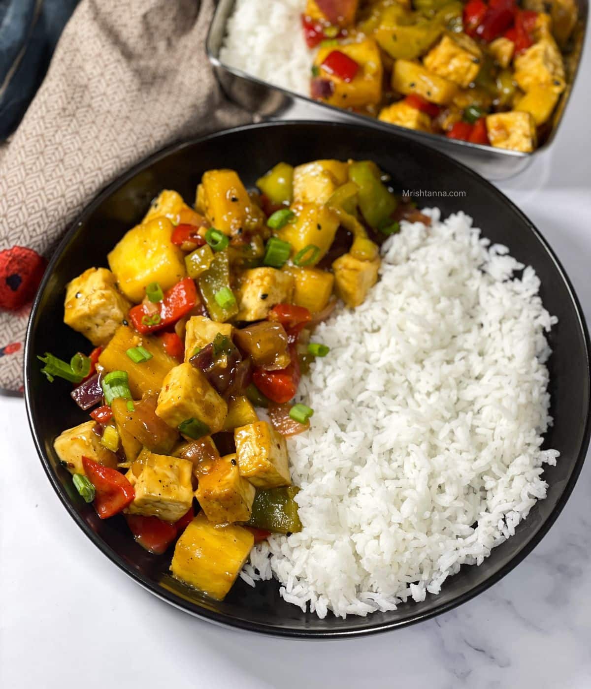 A plate of rice and pineapple tofu stir fry is on the table under the napkins.