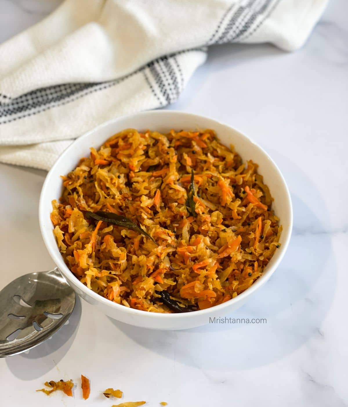 A bowl of mullangi stir fry is on the table with a big spoon.