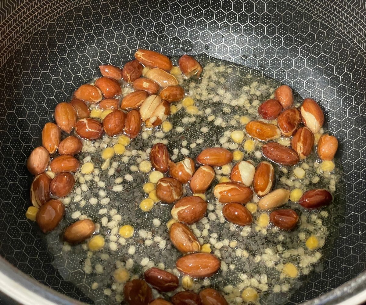 A pot is with whole spices and peanuts frying on heat.
