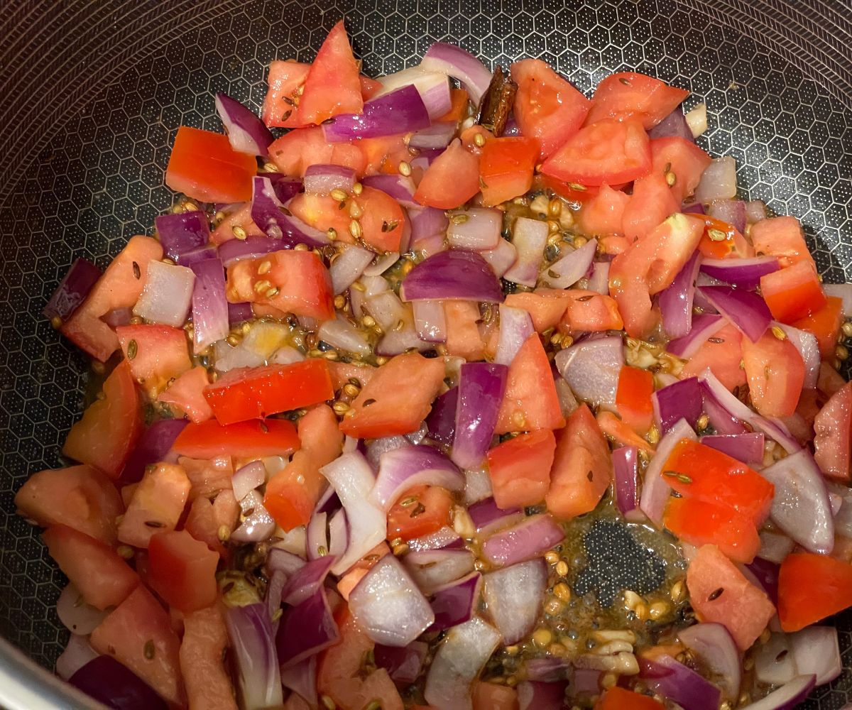 a pan is filled with spices, onions and tomatoes.