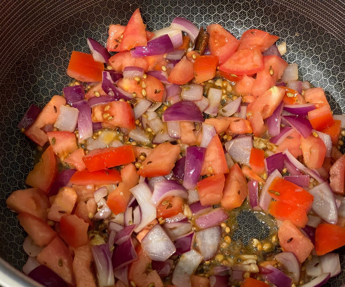 a pan is filled with spices, onions and tomatoes.