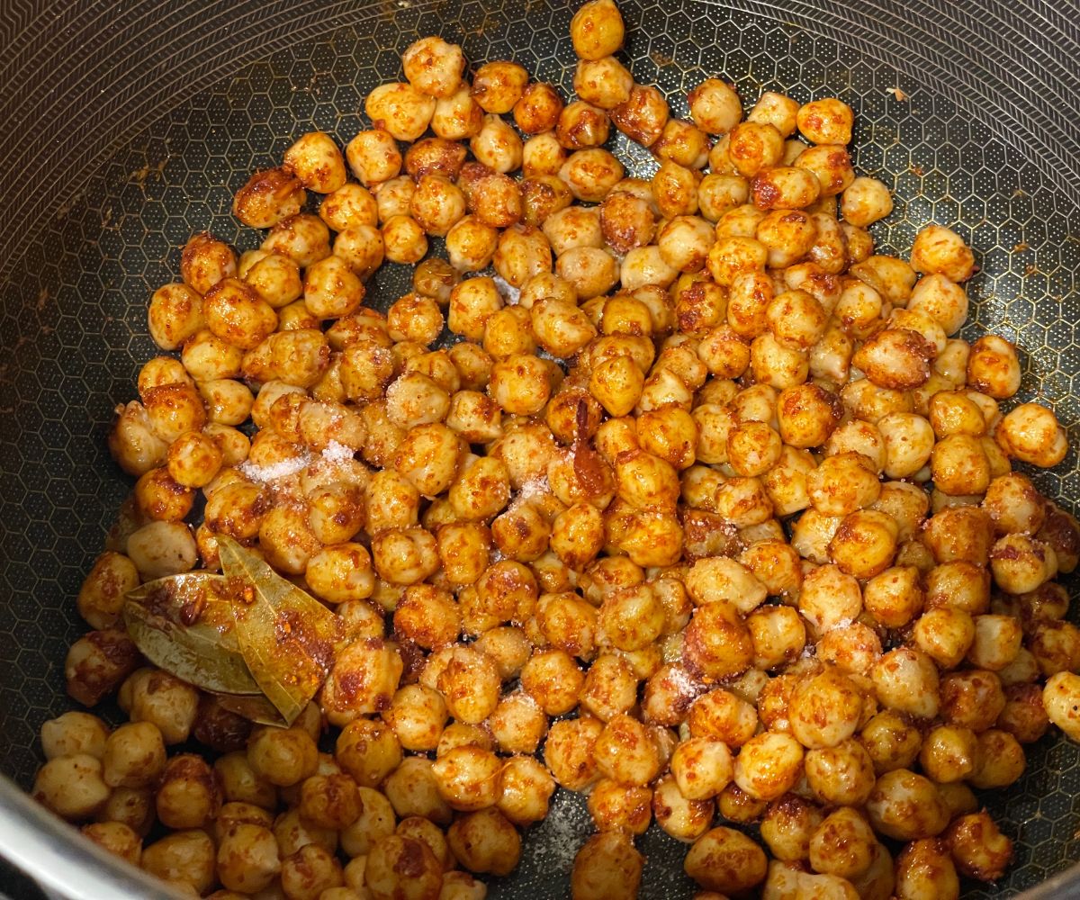 A pot is with spices and cooked chickpeas.