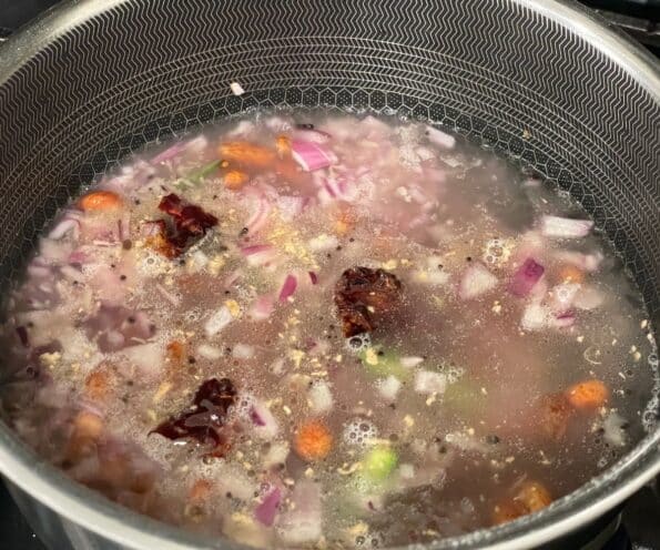 A pot is with boiling water and spices over the heat.