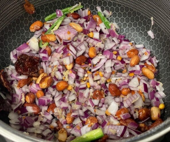 A pot is with spices, onions and green chilies over the flame.