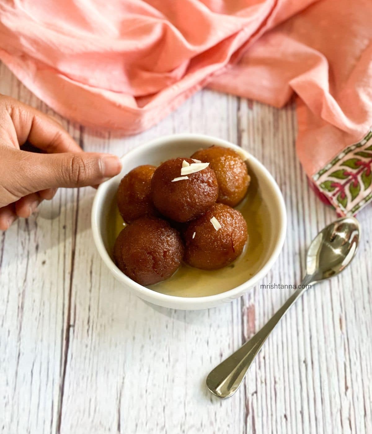 A bowl of Vegan Gulab Jamun is on the table topped with sliced almonds.
