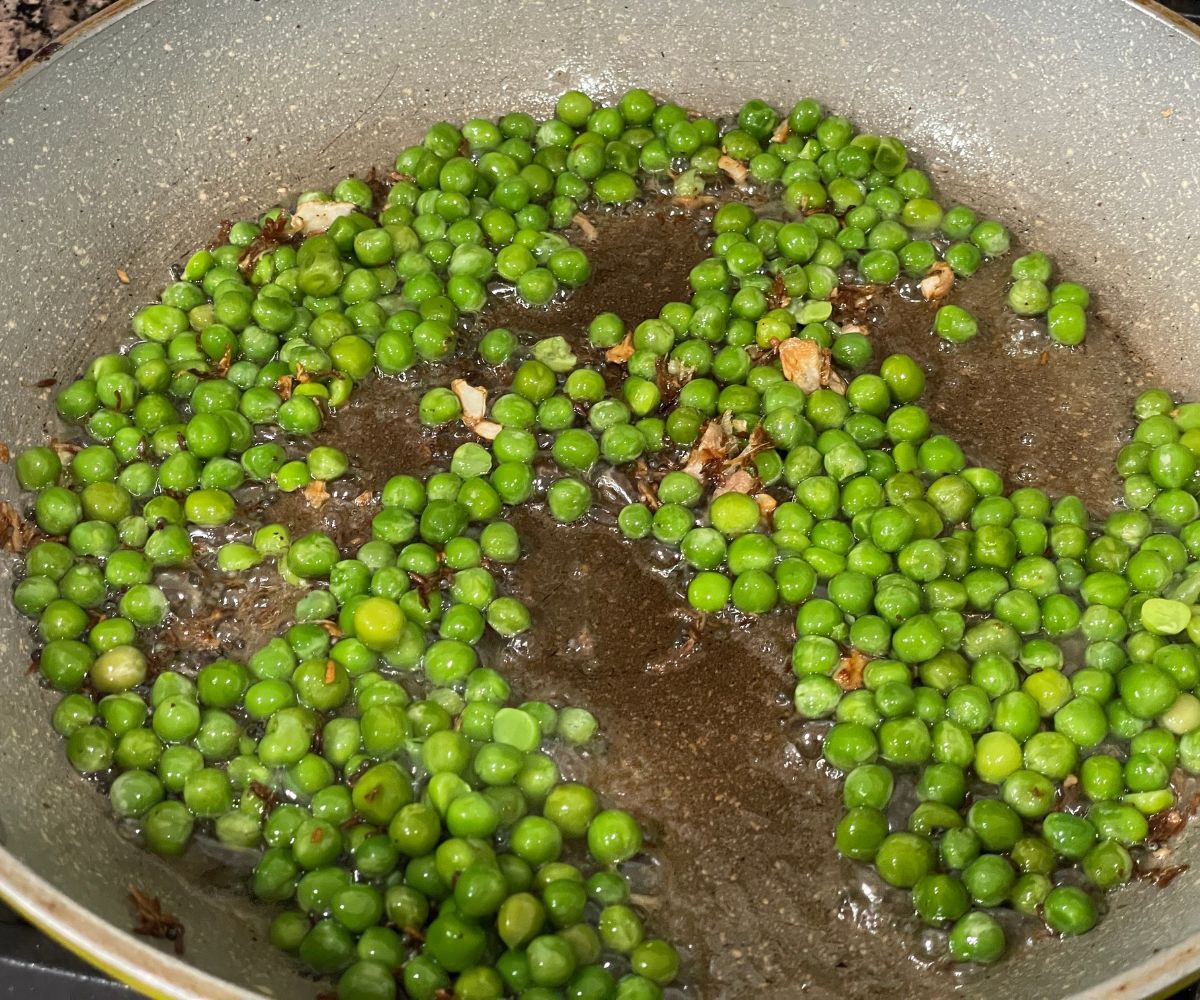 A pan is with green peas and spices over the heat.