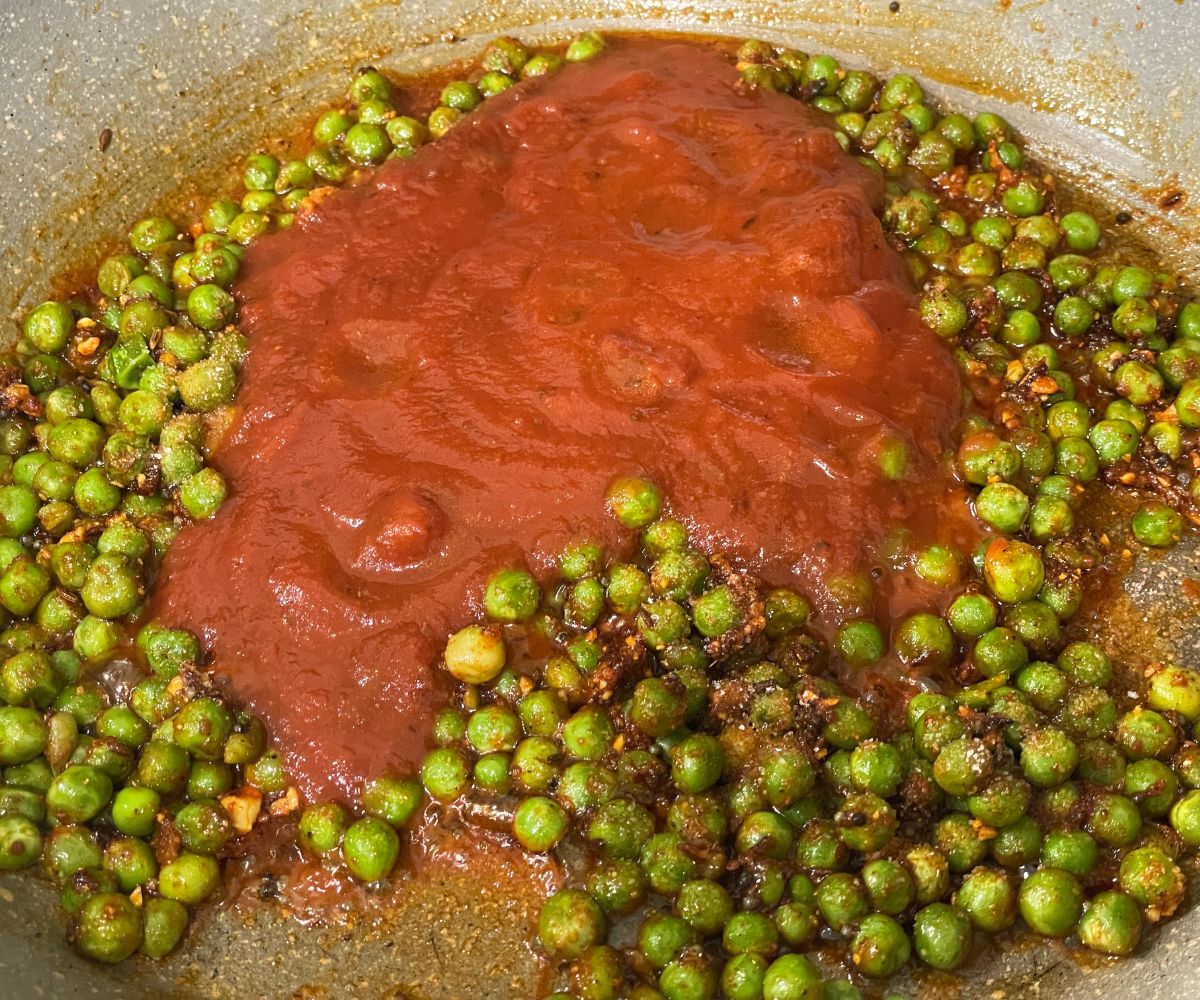 A pan has green peas, tomato puree, and spices.