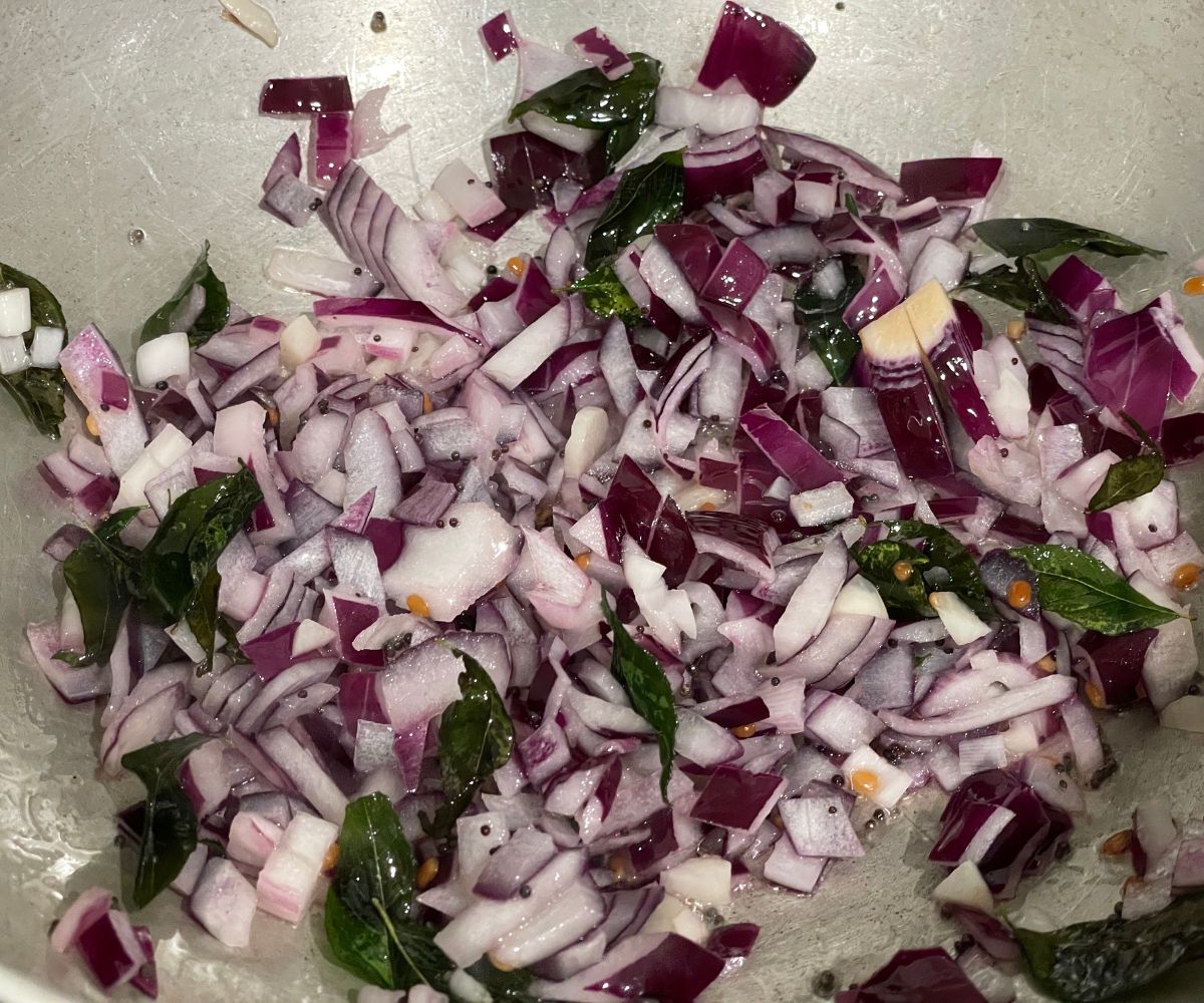 A pot has spices and chopped onions over the heat.