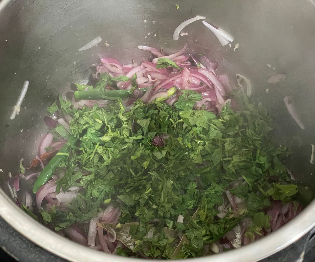 An instant pot is with mint leaves and cilantro for bagara rice.