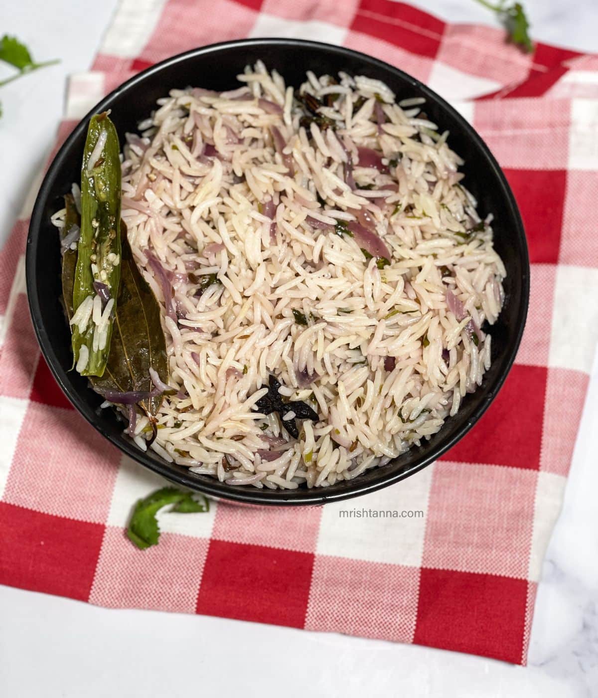 A bowl of bagara rice is on the cotton cloth napkins.