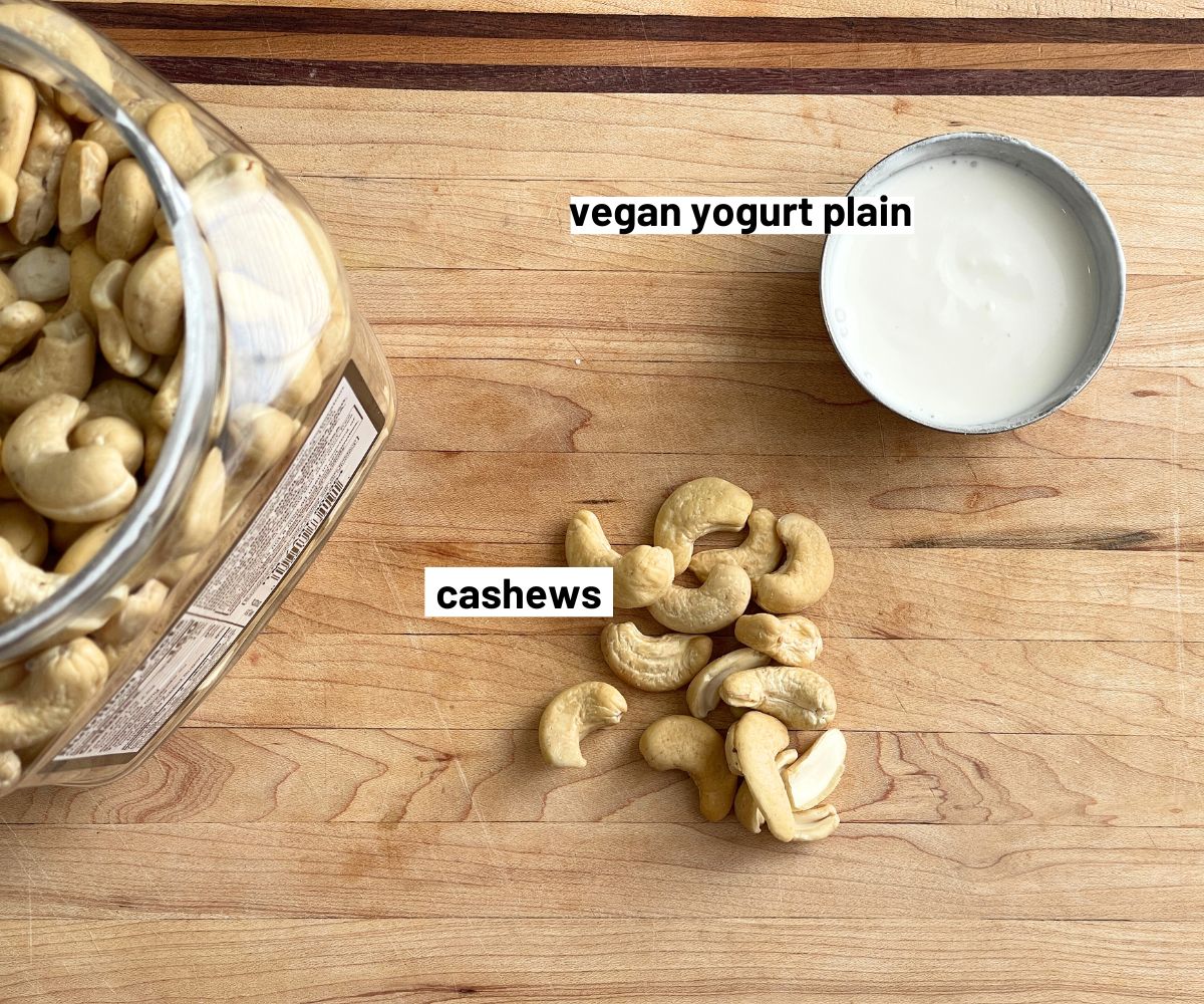 A wooden board has cashews and a bowl of vegan culture.