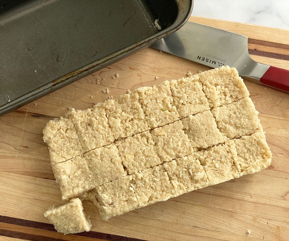 A wooden board is with coconut burfi sweets.