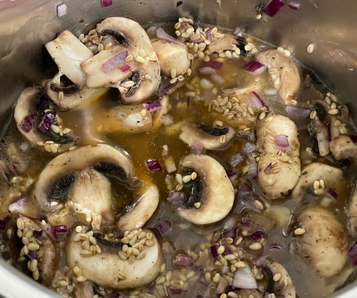 An instant pot filled with barley, vegetable broth and herbs.