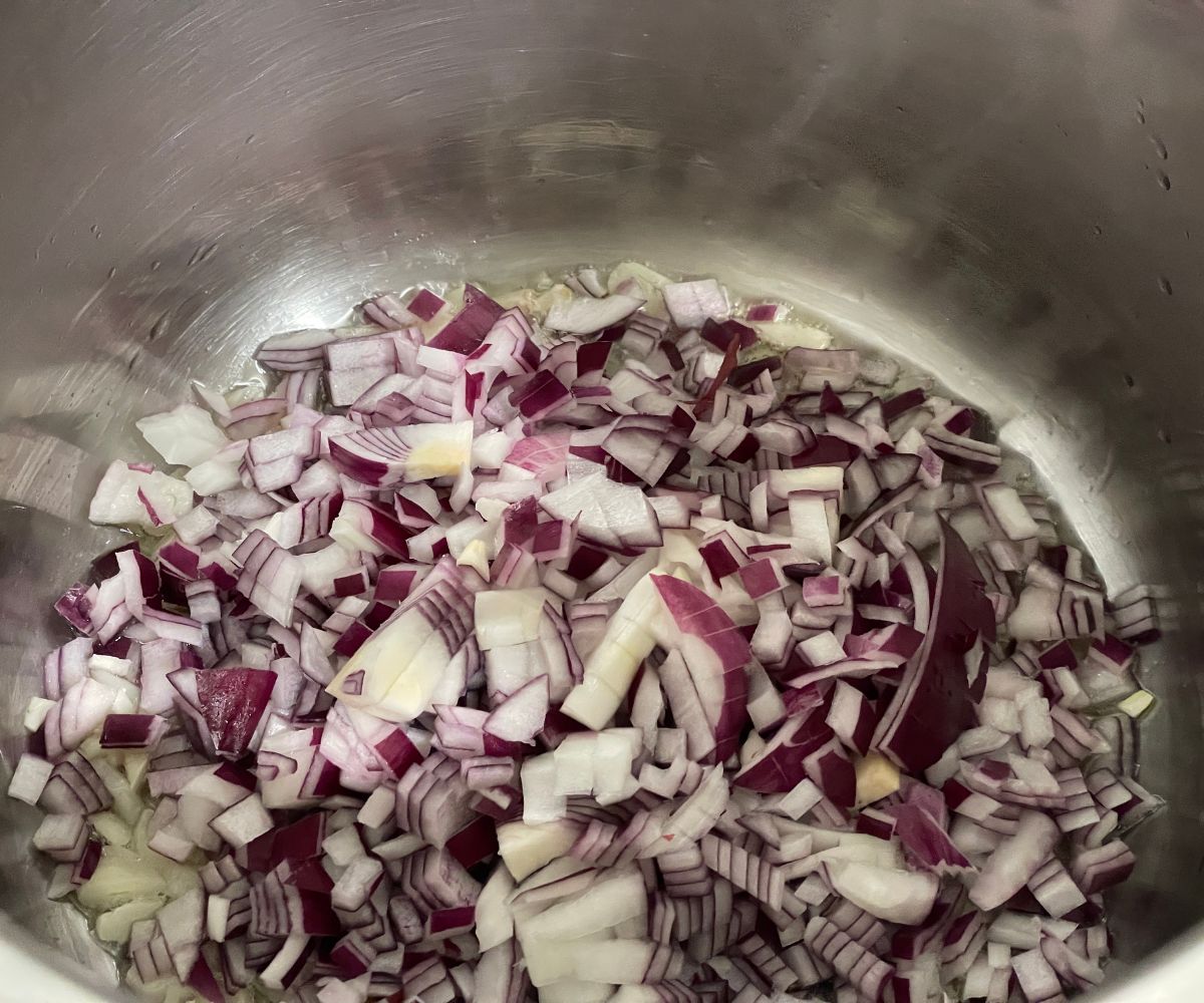 An instant pot is with chopped onions and garlic.