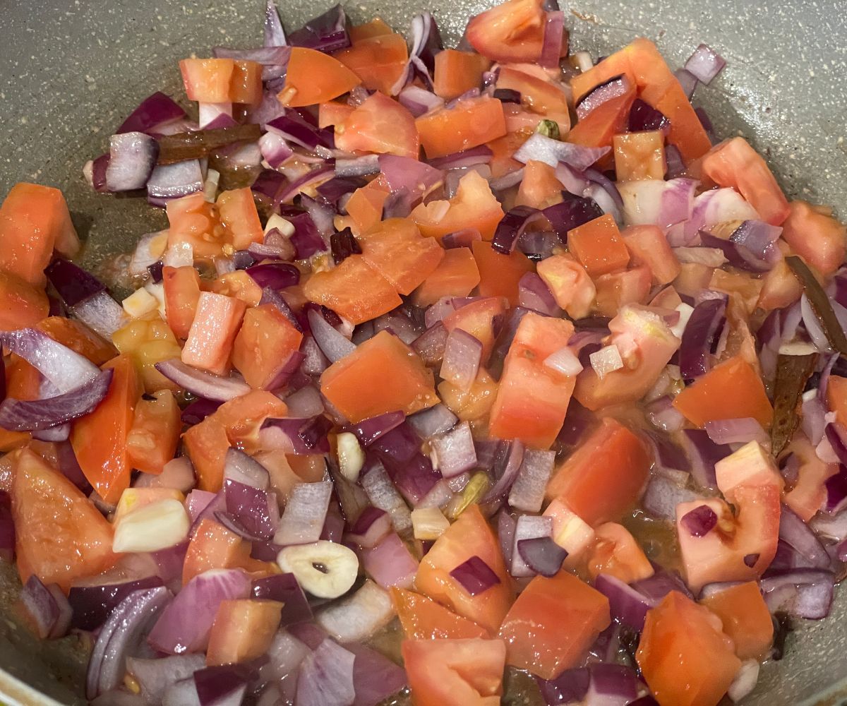 A pan is filled with onions, garlic and tomatoes for curry base.