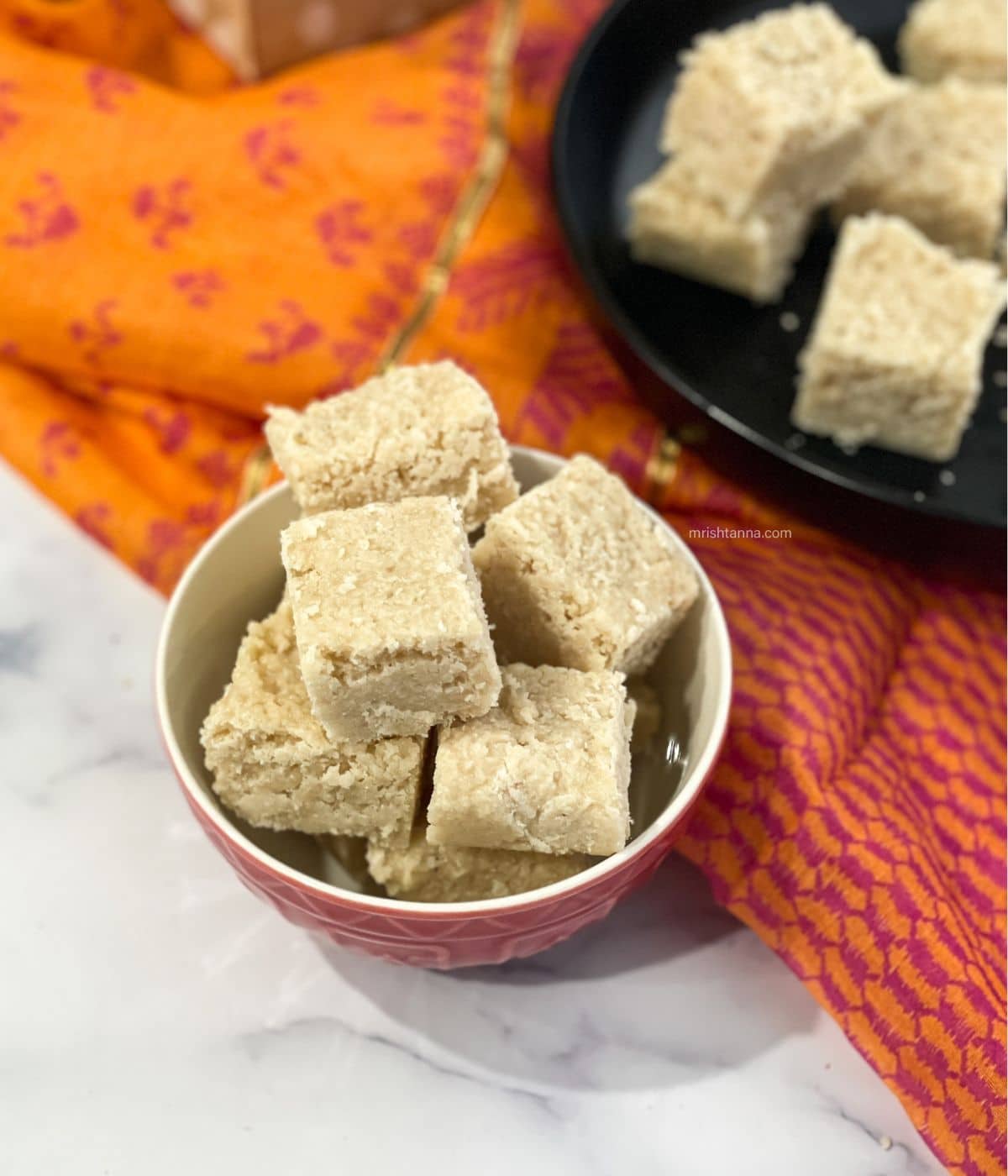 A bowl of thengai burfi is on the table.