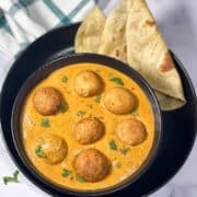 A bowl of vegan malai kofta curry is on the plate with chapati.