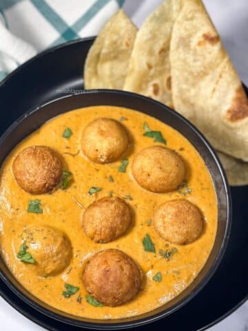 A bowl of vegan malai kofta curry is on the plate with chapati.