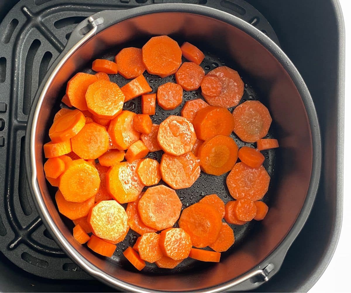 Air fryer basket has sliced carrots.