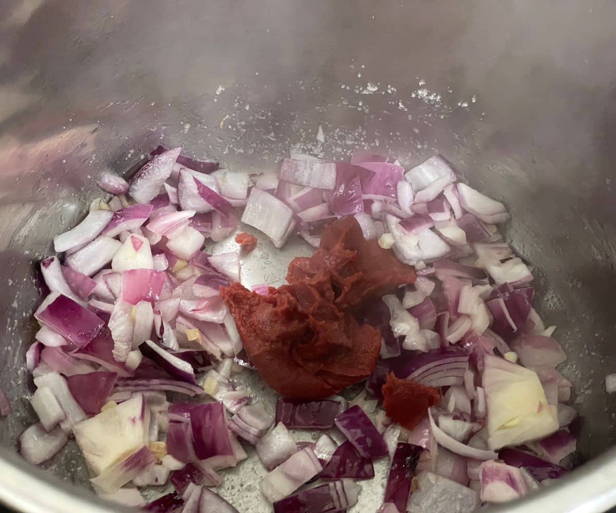 An instant pot has tomato paste along with onions.