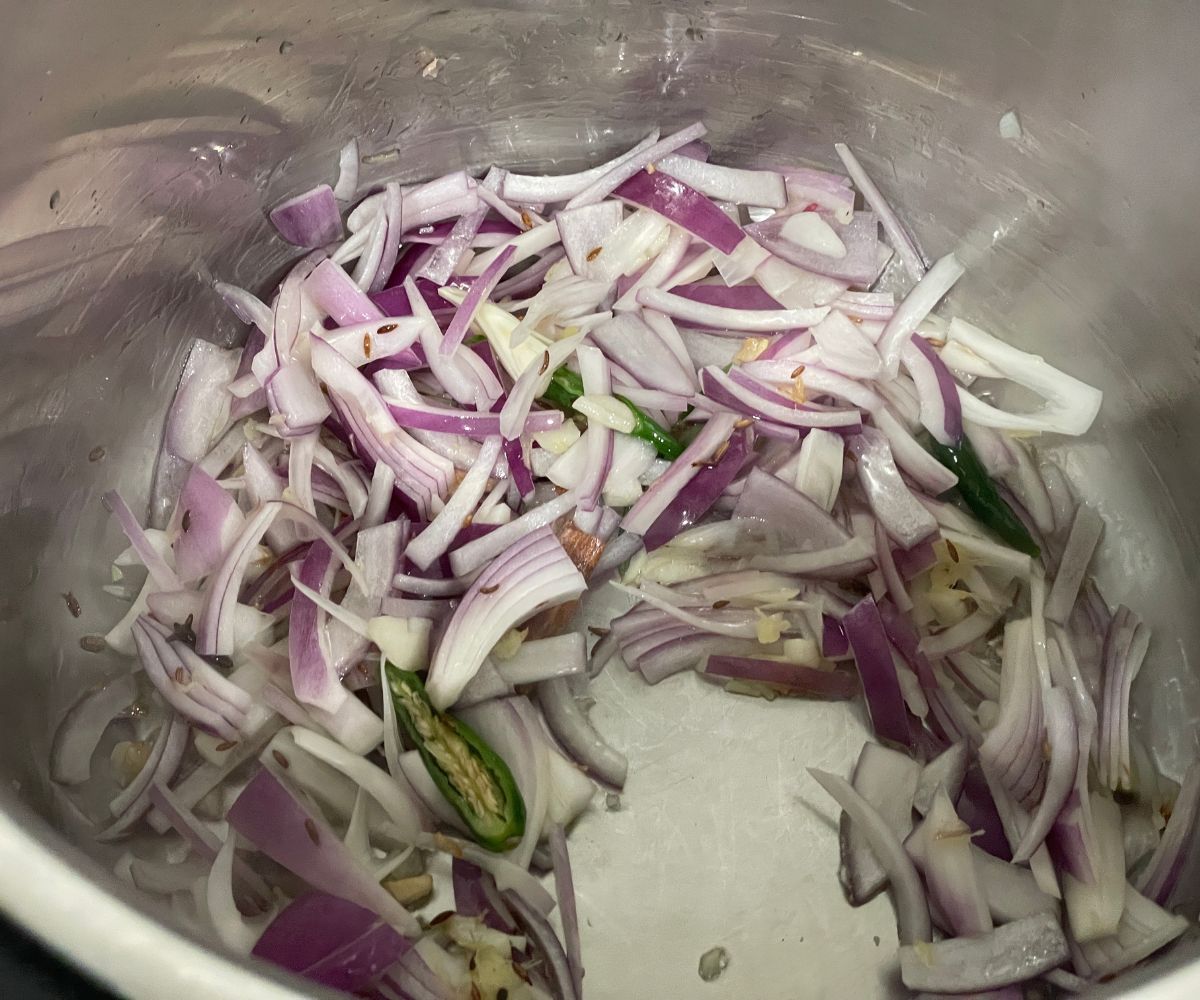 An instant pot has spices, ginger, and onions in saute mode.