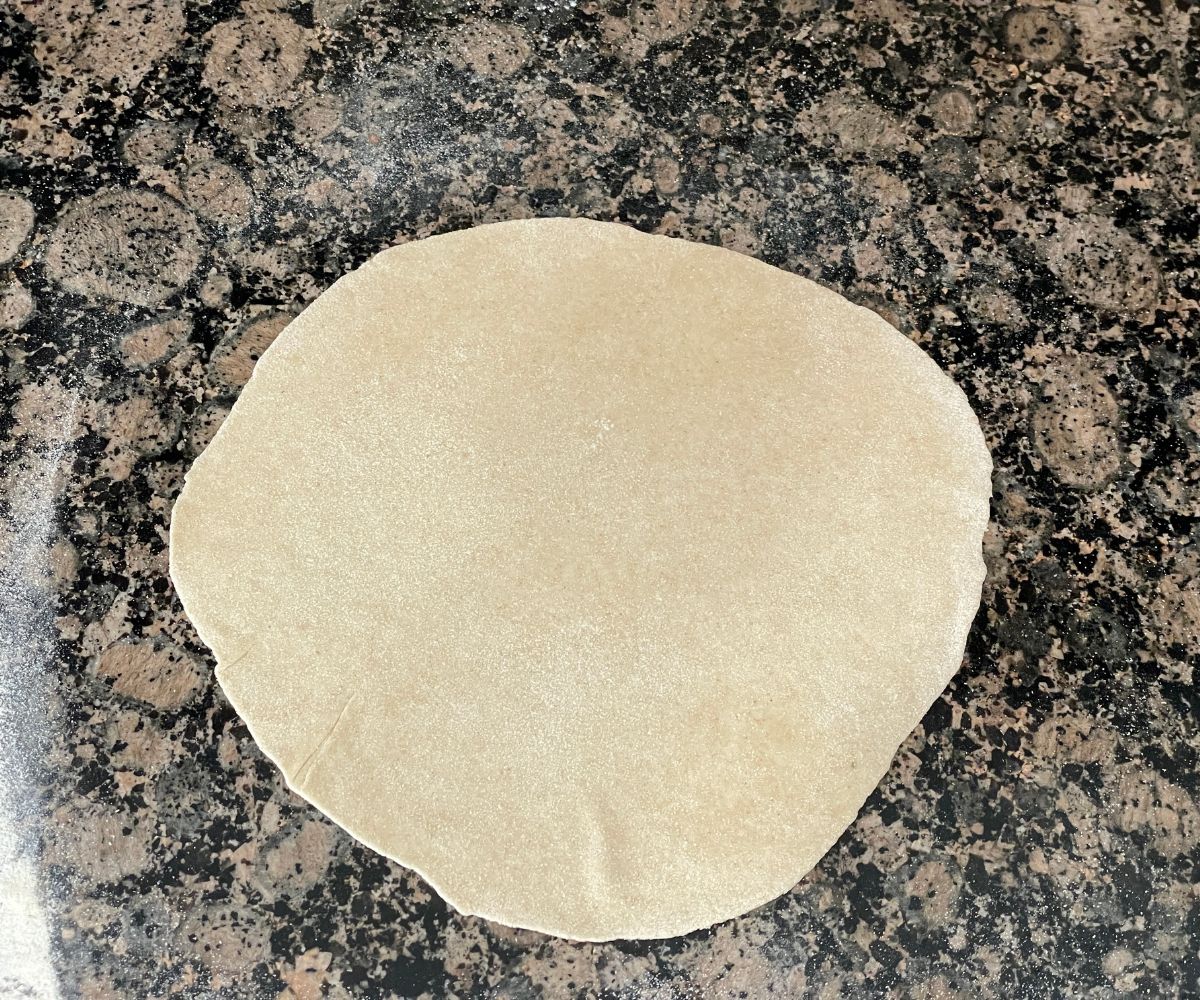 A rolled chapati dough is on the surface.