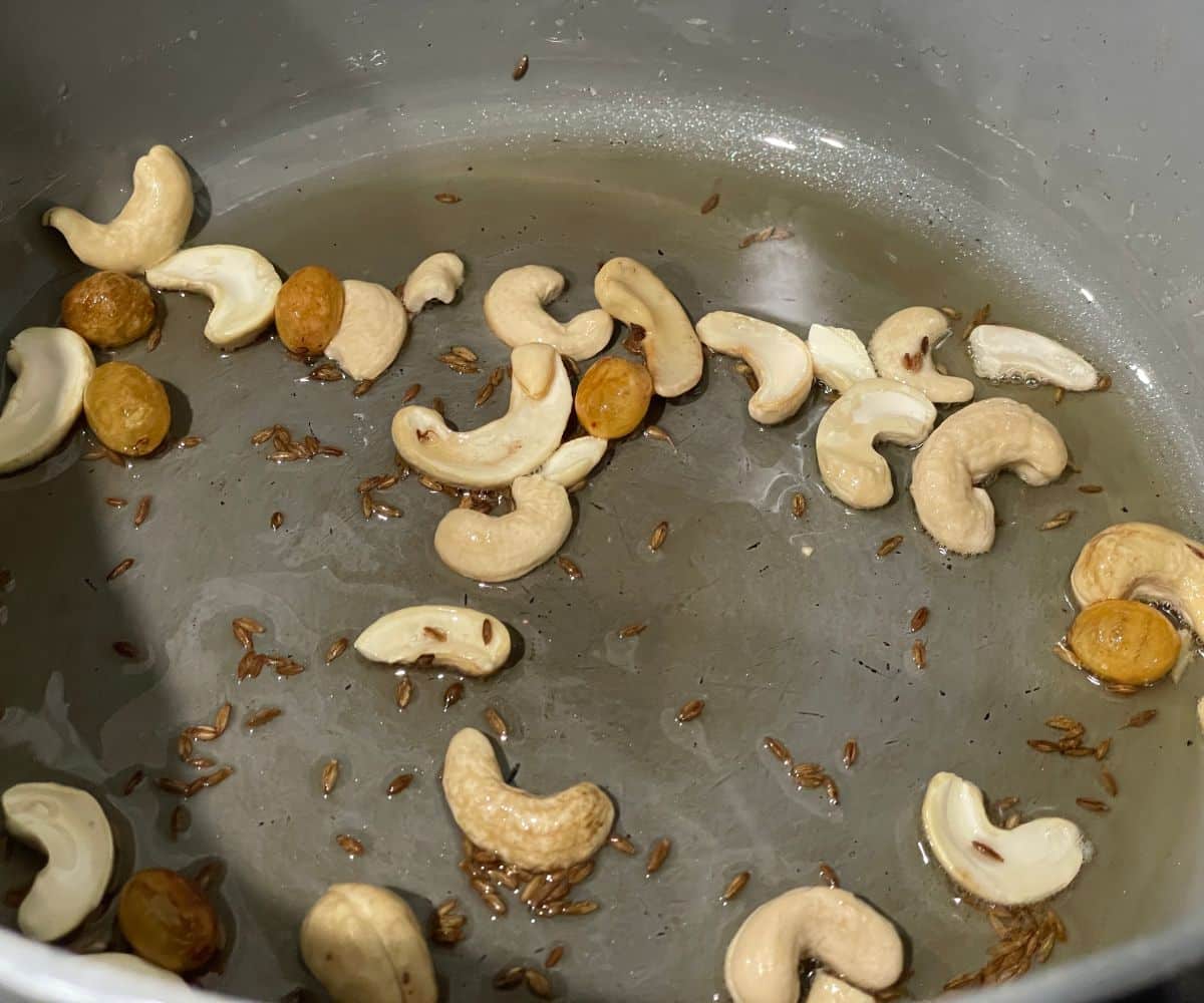 A pot is with oil, cumin seeds and cashews.