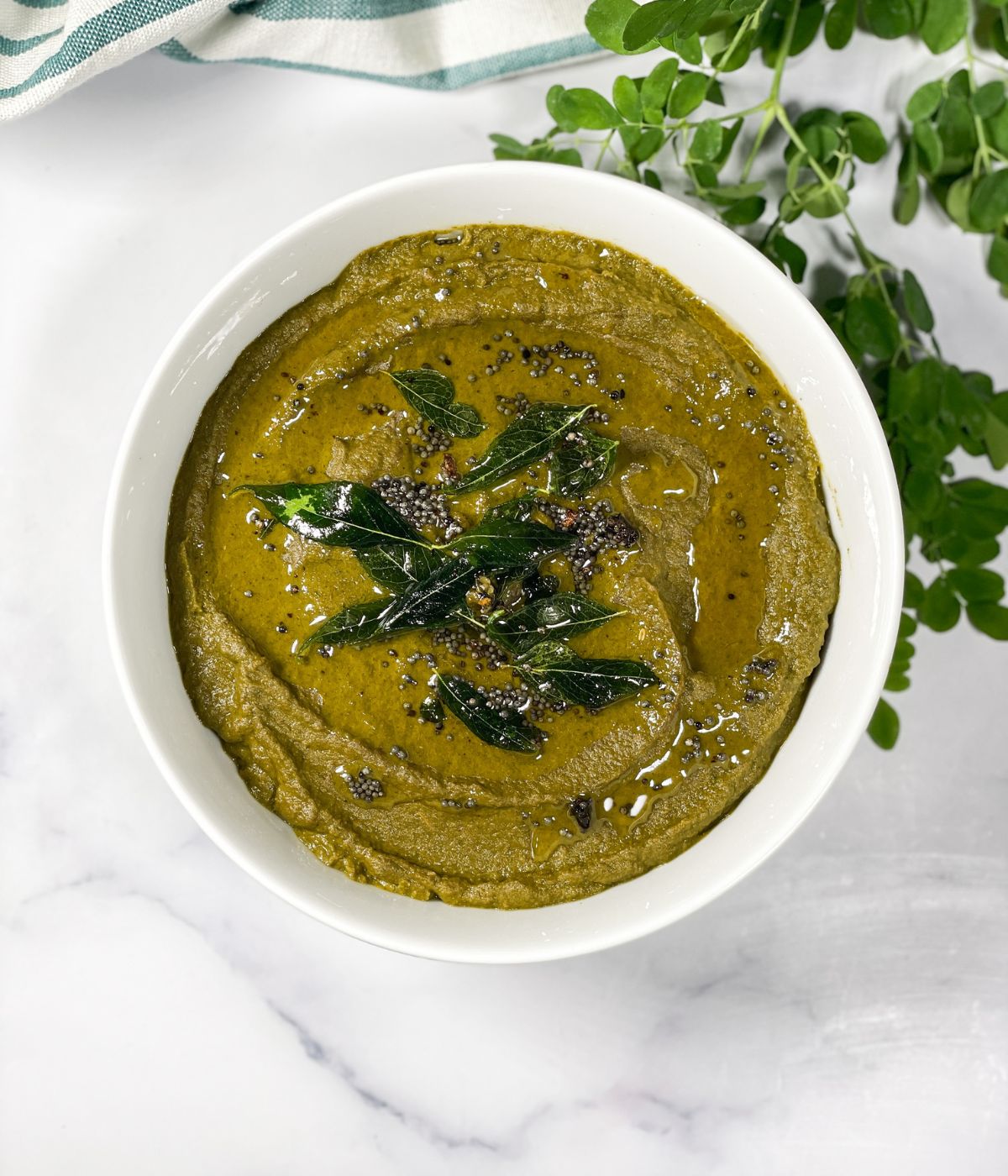 A bowl is full of moringa leaves chutney.