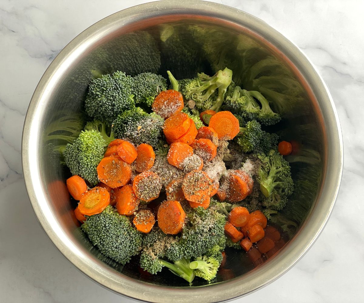 A bowl has broccoli florets, seasonings, and air fried carrots.
