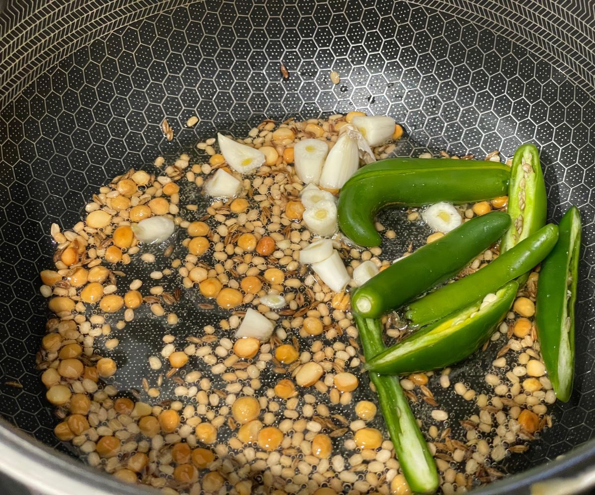 A pot has oil, and whole spices on the stove top.