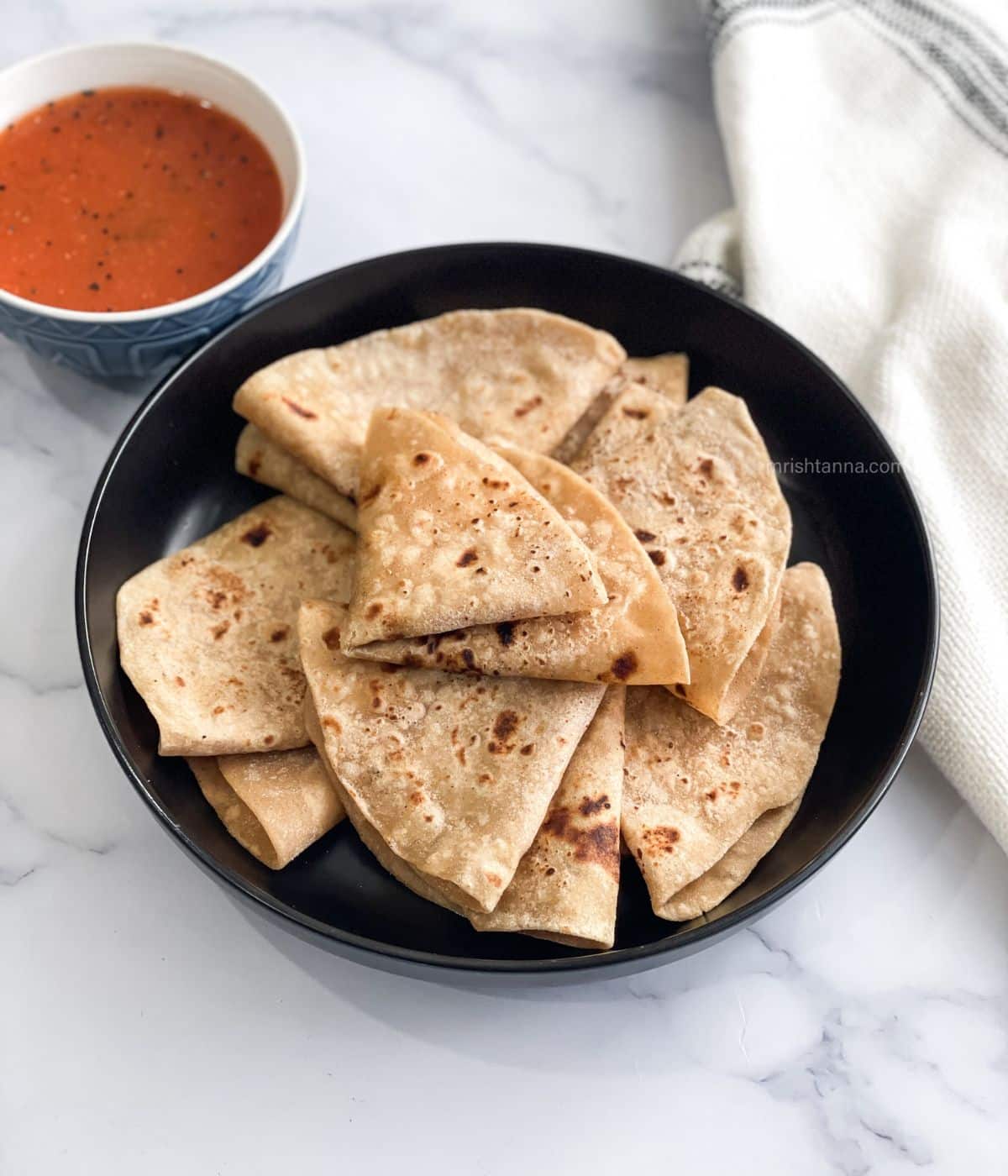 A plate has folded chapati's  and a bowl of curry.