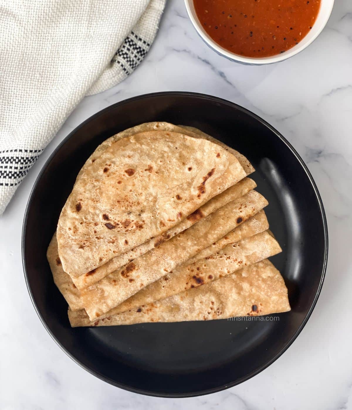 A plate has a stack of soft chapati's.