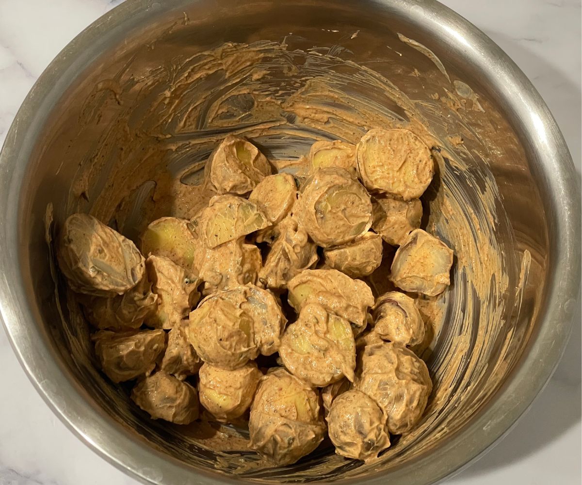 A bowl of marinated potatoes is on the counter top. 