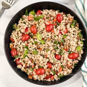 A plate has vegan barley salad with vegetables.