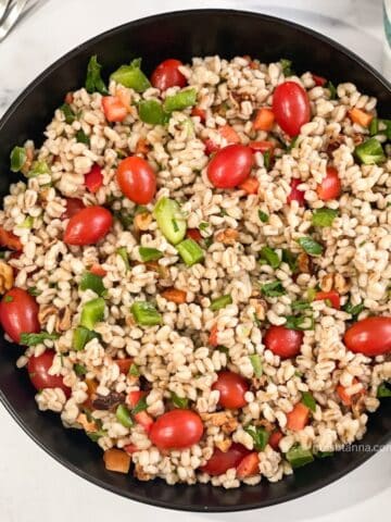 A plate has vegan barley salad with vegetables.