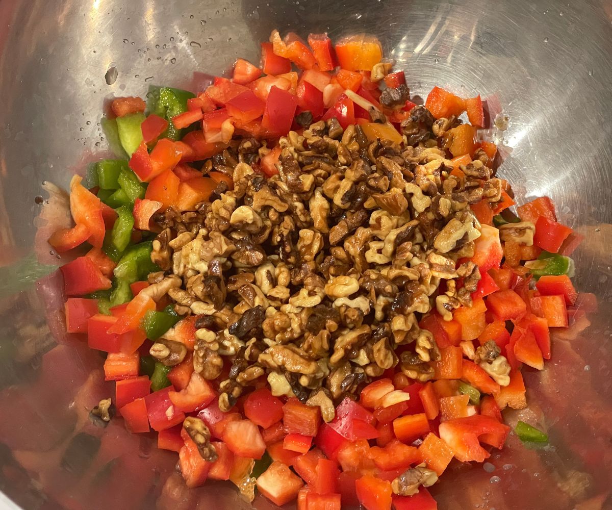 A bowl has chopped vegetables and toasted walnuts.