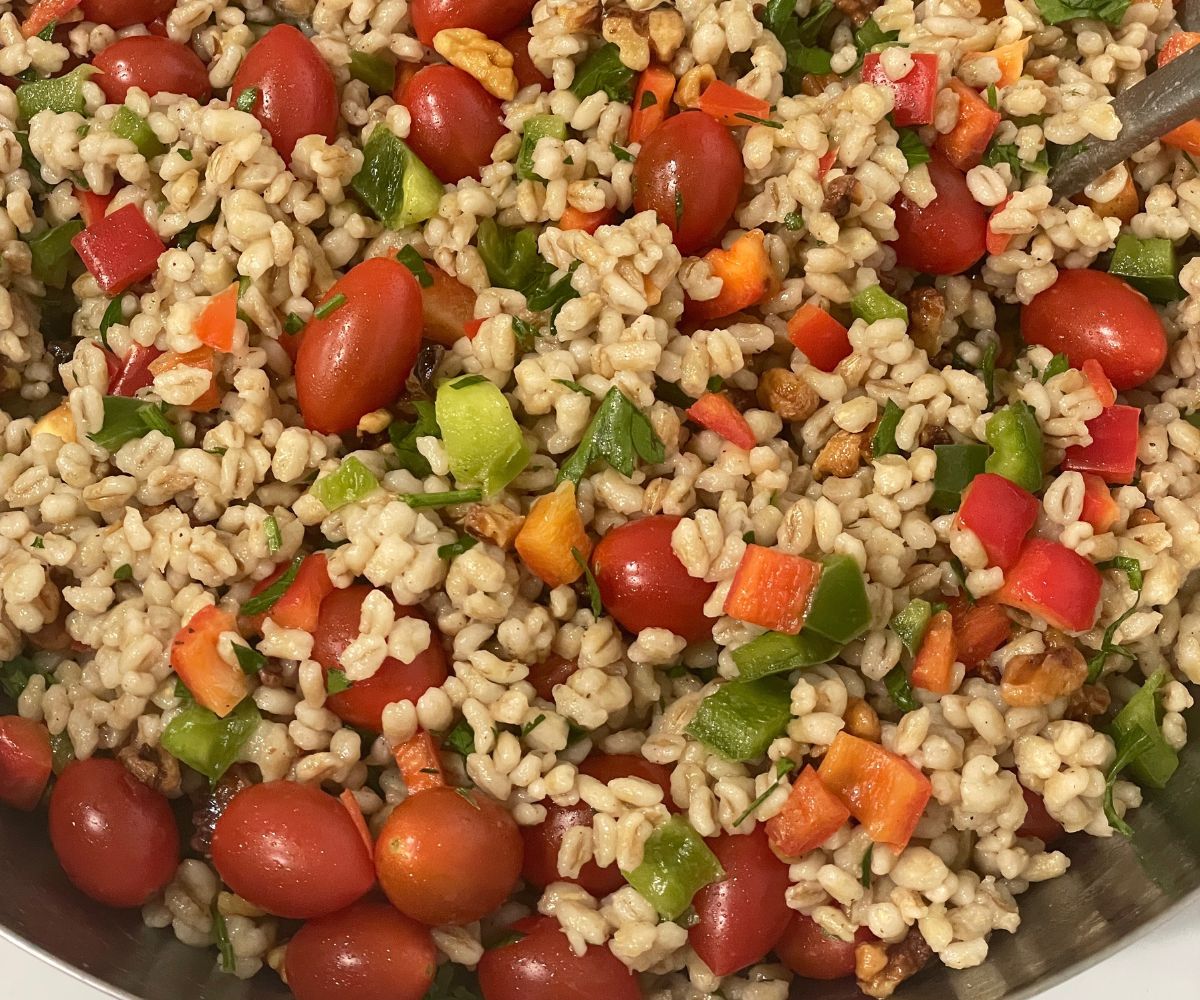 A bowl has vegan barley salad with vegetables.