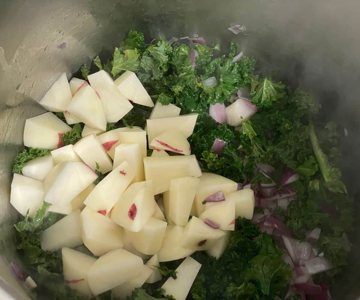 An instant pot has chopped kale, onions, onions on saute setting.