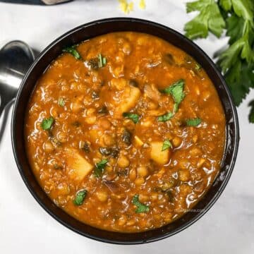 A bowl is full of vegan lentil soup and topped with chopped parsley.