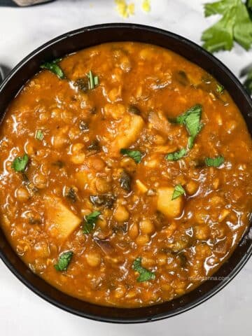 A bowl is full of vegan lentil soup and topped with chopped parsley.