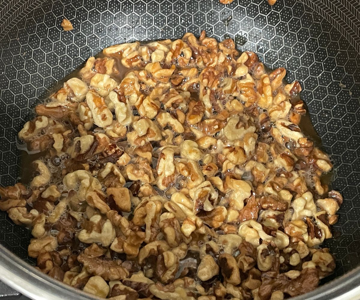 A heated pan is with chopped walnut and oil.