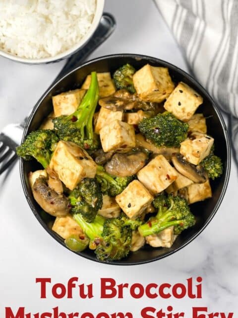 A bowl of stir fried tofu broccoli and mushrooms is on the table.