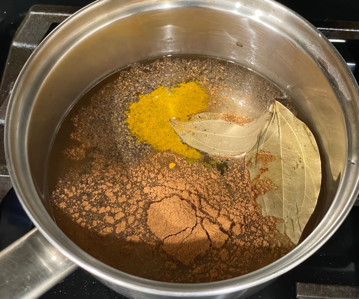 A pot has water, bay leaves and cinnamon powder on the stove top.